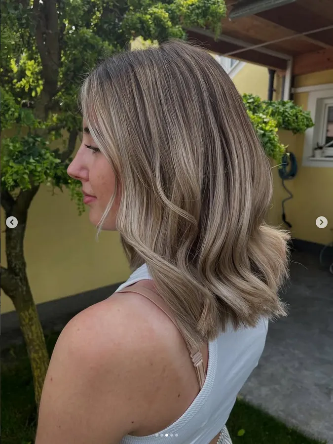 Schulterlanger, gewellter Bob in Blond mit dunklerem Ansatz, im Freien fotografiert
